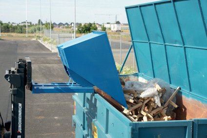 En blå container med träavfall och plastpåsar i en inhägnad utomhusmiljö.