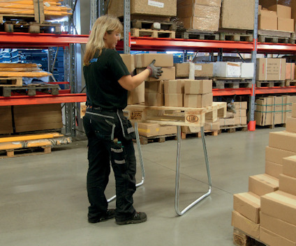 Person staplar kartonger på ett bord i ett lager med hyllor och paket runtomkring.