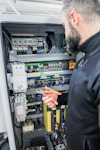 En person arbetar med elektriska komponenter i ett öppet skåp, håller en tång i handen.