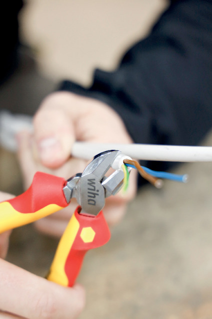 En person håller en avbitartång från Wiha och klipper av en kabel med flera kopparledare.