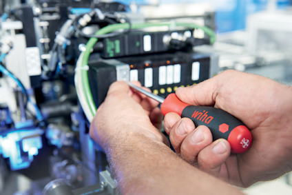 Händer håller en röd och svart skruvmejsel och arbetar på elektroniska komponenter med gröna kablar.