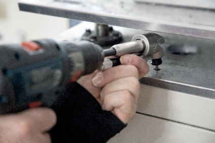 En person använder en borrmaskin med en socket fäste på en metalldel.