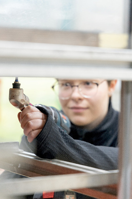 En person med glasögon borrhåller en metallstruktur med en handborr.