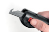 Säkerhetskniv med svart handtag och röd knapp hålls av en hand.