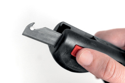 Säkerhetskniv med svart handtag och röd knapp hålls av en hand.