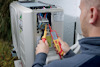 En person använder en digital multimeter för att mäta spänning i ett luftkonditioneringssystem.