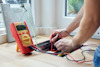 En person använder en digital multimeter för att mäta spänning i eluttag i ett golv.