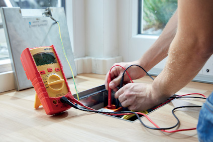 En person använder en digital multimeter för att mäta spänning i eluttag i ett golv.