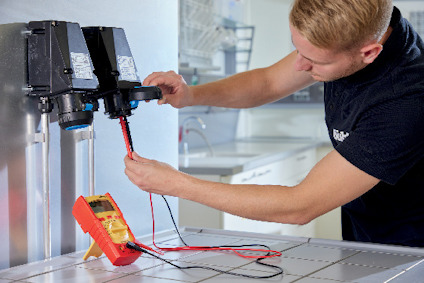 Person testar elektriska kontakter med en multimeter vid en metallbänk.