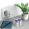 Vägguttag med USB-adapter som laddar två stora batterier. En krukväxt och en anteckningsbok med penna syns bredvid.