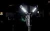 Svart ställbar arbetslampa med tre LED-paneler som lyser i en mörk omgivning.