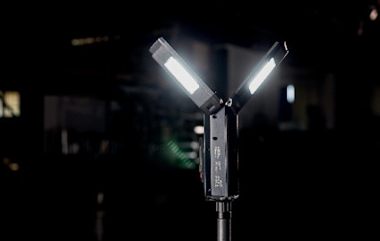 Svart ställbar arbetslampa med tre LED-paneler som lyser i en mörk omgivning.