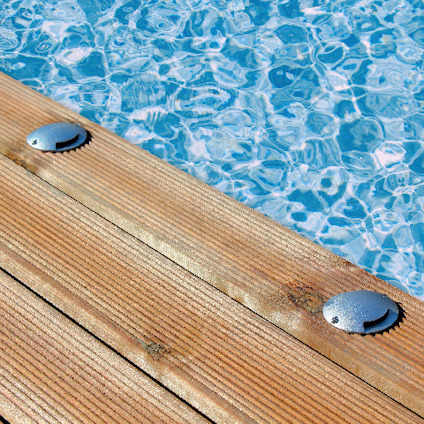 Trätrall intill en pool med turkost vatten, solbelyst med två metallavlopp synliga på trallen.