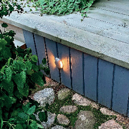 Träaltan med lysande lampa på sidan, omgiven av gröna växter och stenar på marken.