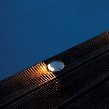 Nedsänkt rund lampa i trätrall, sänder ut varmt ljus mot den mörka ytan.