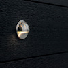 Runt väggljus med metallfinish monterat på svart träpanel.