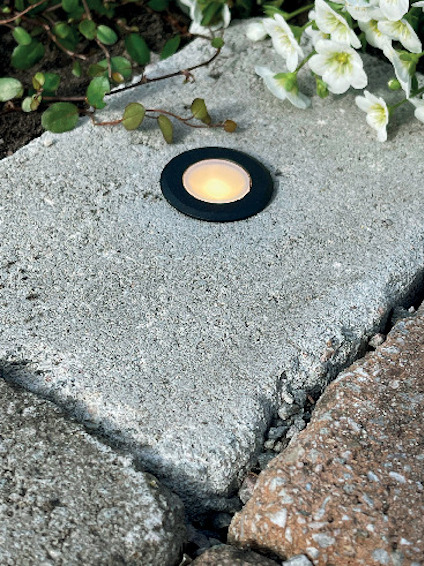 Marksten med en inbyggd rund lampa omgiven av blommor och växter.