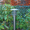 Utomhuslampa i metall med grenar och gröna blad i bakgrunden.