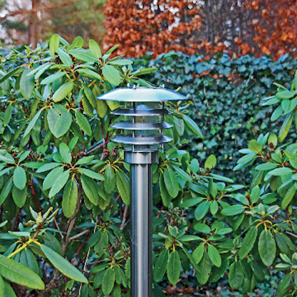 Utomhuslampa i metall med grenar och gröna blad i bakgrunden.
