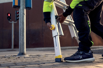 Person i arbetskläder håller en stege på trottoaren nära en stopplyktspol och ett trafikljus.