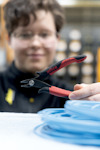 Person håller i en röd och svart avbitartång framför en blå kabel.