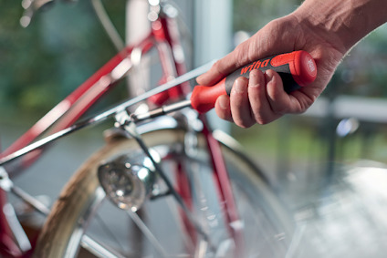 Hand håller en skruvmejsel nära en röd cykel.
