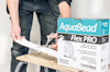 Person klipper AquaBead Flex PRO-produkt från en kartong på en träbänk.