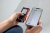 Person som håller en avståndsmätare och en smartphone med en app som visar mätresultat.