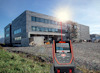 Laseravståndsmätare riktad mot en byggnad med lager av byggställningar och en klar himmel i bakgrunden.