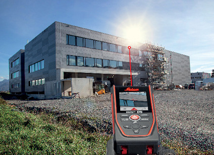 Laseravståndsmätare riktad mot en byggnad med lager av byggställningar och en klar himmel i bakgrunden.