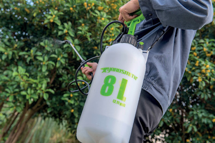 En person håller en vit 8-liters spruta med svart och grön pumpmekanism.