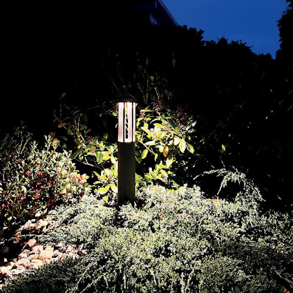 Trädgårdslampa omgiven av grönska och buskar under kvällstid.