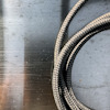 Flätad metallslang på en grå, polerad metallisk yta.