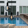 Två glödlampsformade lampor hänger över en pool med trädäck, moderna byggnader i bakgrunden.