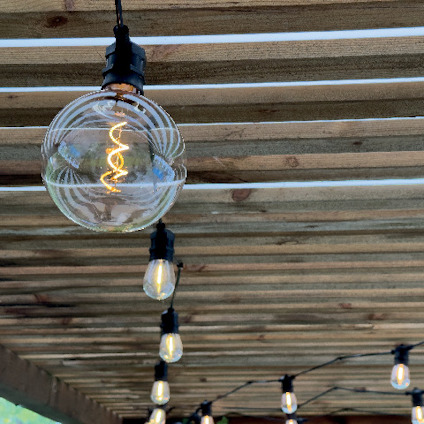 Glödlampa med synliga glödtrådar hänger under ett trätak. Flera lampor i rad.