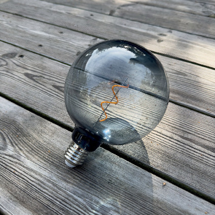 Glödlampa med spiralformad glödtråd på en träveranda.