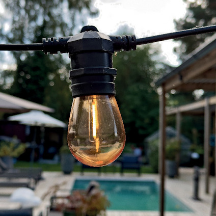 Hängande glödlampa utomhus med suddig bakgrund av träd och en pool.
