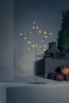 Stjärnformad ljusdekoration med liten lampa, äpplen och furucones på en betongyta.