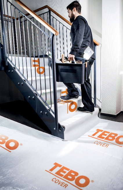 Person går uppför trappa täckt med vit skyddsfolie märkt "TEBO COVER".