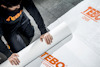 Person rullar ut vit materialduk med orange text "TEBO COVER".