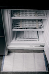 Öppen kyl eller frys med frostfri teknik, isbildning och fuktuppsamlingsmatta på golvet framför.