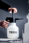 En person pumpar med en handpumpad spruta märkt "TEBO". Bakgrunden är delvis suddig.