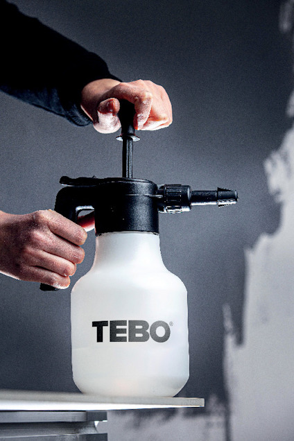 En person pumpar med en handpumpad spruta märkt "TEBO". Bakgrunden är delvis suddig.