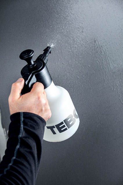Hand som sprayar vatten på en vägg med en vit och svart sprayflaska märkt "TEBO".