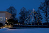 Modernt hus med stora fönster, snötäckt mark och upplysta träd i bakgrunden i skymningen.