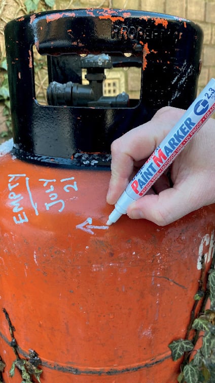 En hand märker en orange gastub med en vit penna. Text på tuben: "Empty July 21" och en pil pekar uppåt.