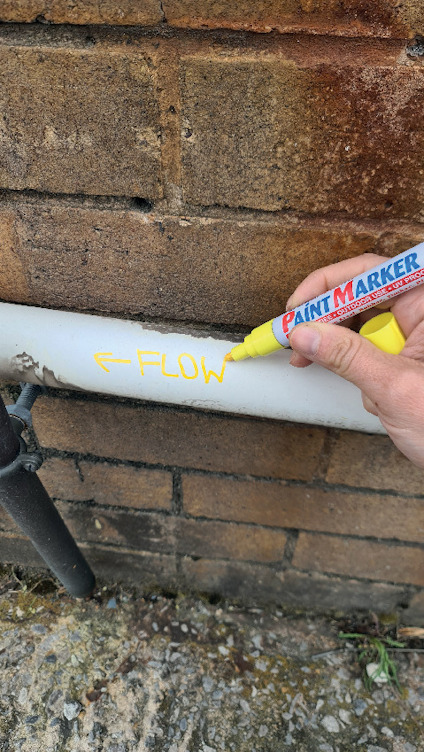 Hand skriver "FLOW" med gul färgpenna på ett vitt rör mot en tegelvägg.