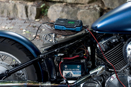 Motorcykel med batteriladdare ansluten till BLEI-GEL BATTERIE, placerad nära bakhjulet.
