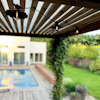 Pergola med hängande lampor, bakom syns en pool, grönska och ett hus i bakgrunden.