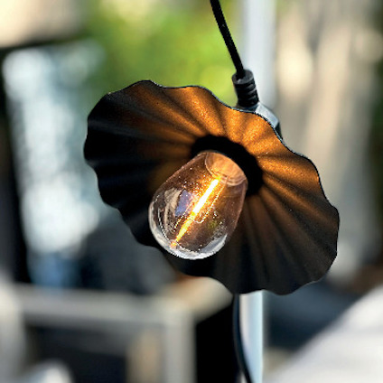 Svartlampskärm med synligt glödlampa upphängd på en sladd mot en suddig bakgrund.